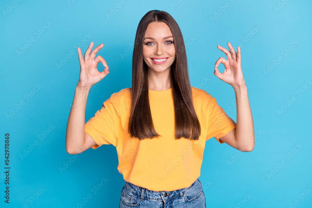 Photo of adorable pretty stylish lady raise two hand arm show okey symbol good job shop stand empty space isolated on blue color background Photo of adorable pretty stylish lady raise two hand arm show okey symbol good job shop stand empty space isolated on blue color background