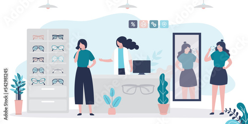 Woman chooses sunglasses. Female consumer stands at mirror and fitting new eyeglass for purchase. Optometrist shelping client. Fashion optics store. Shopping, consumption concept.