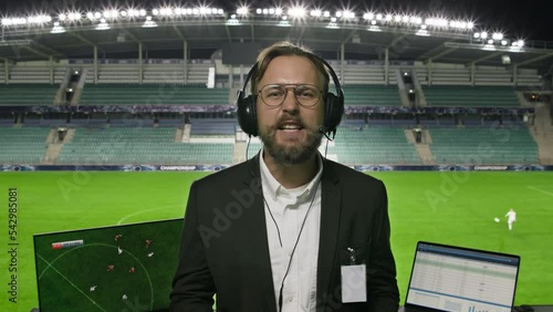 Portrait of Sports Commentator Analysing Soccer Match. POV Shot: Professional Announcer with Football Stadium and Field Behind Him Commenting on the Seasons Best Moments, Talking about Top Players photo