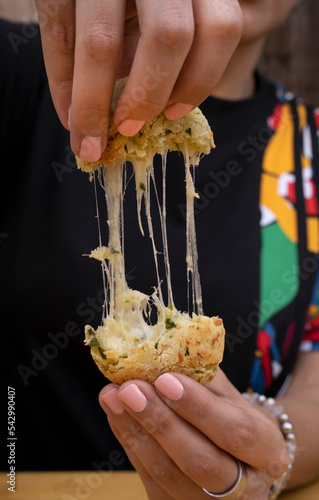 Closeup view of a woman's hands stretching the hot cheese of a small, baked, provolone flavored roll, called chipa.  photo