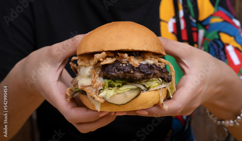 Monster burger. Woman holding a multilayer hamburger with mozzarella cheese, meat, cucumber pickles, mayonnaise, lettuce and crispy onion.