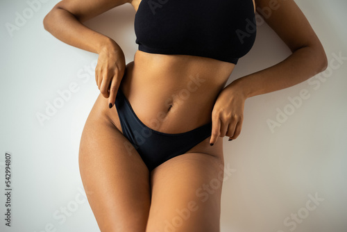 Cropped view of sexy african american woman in crop top touching black panties near wall at home.