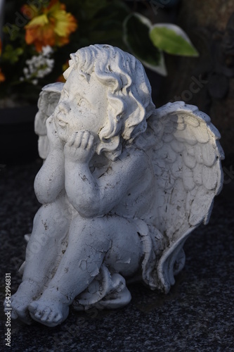 Petite statue d'un ange aux cheveux bouclés qui est assis l'air pensif, les coudes posés sur les genoux et la tête un peu relevée dans la paume de ses mains photo