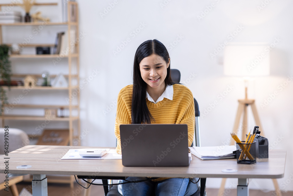 Image of young Business Asian woman work on laptop and calculator sitting at the desk indoors in home office, doing math finance tax, report, accounting, statistics, and analytical research concept. Image of young Business Asian woman work on laptop and calculator sitting at the desk indoors in home office, doing math finance tax, report, accounting, statistics, and analytical research concept.