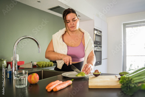 Low angle view of the happy lady chopping avocado while cooking in kitchen