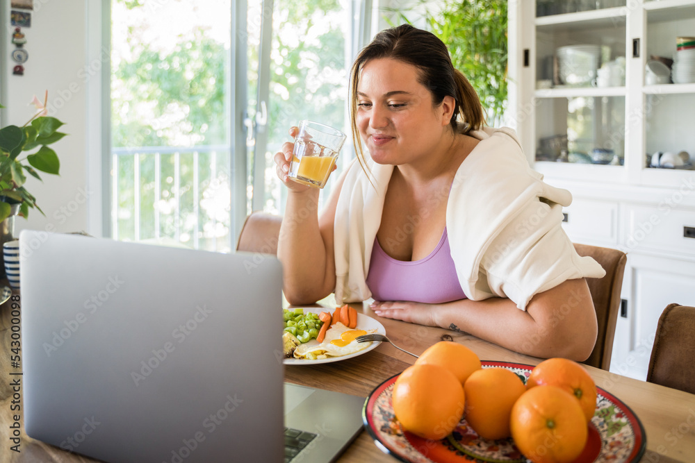 Beautiful young body positive woman eating her meal and watching movie at the laptop