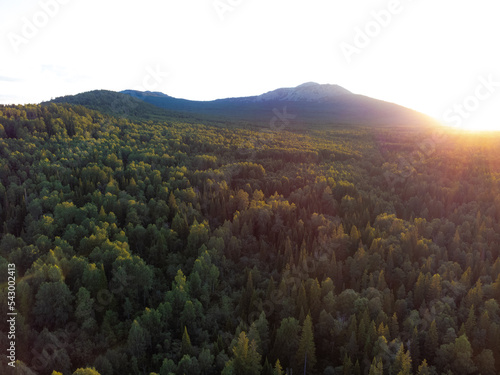 Aerial view of mountain range and forest with sun setting behind the mountain