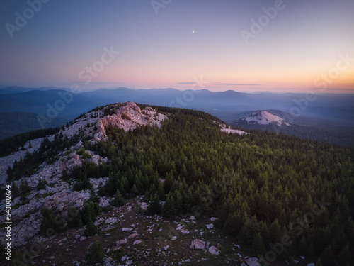 Aerial view of mountain range in the dusk with the crescent moon in the sky and mountains on the distant horizon