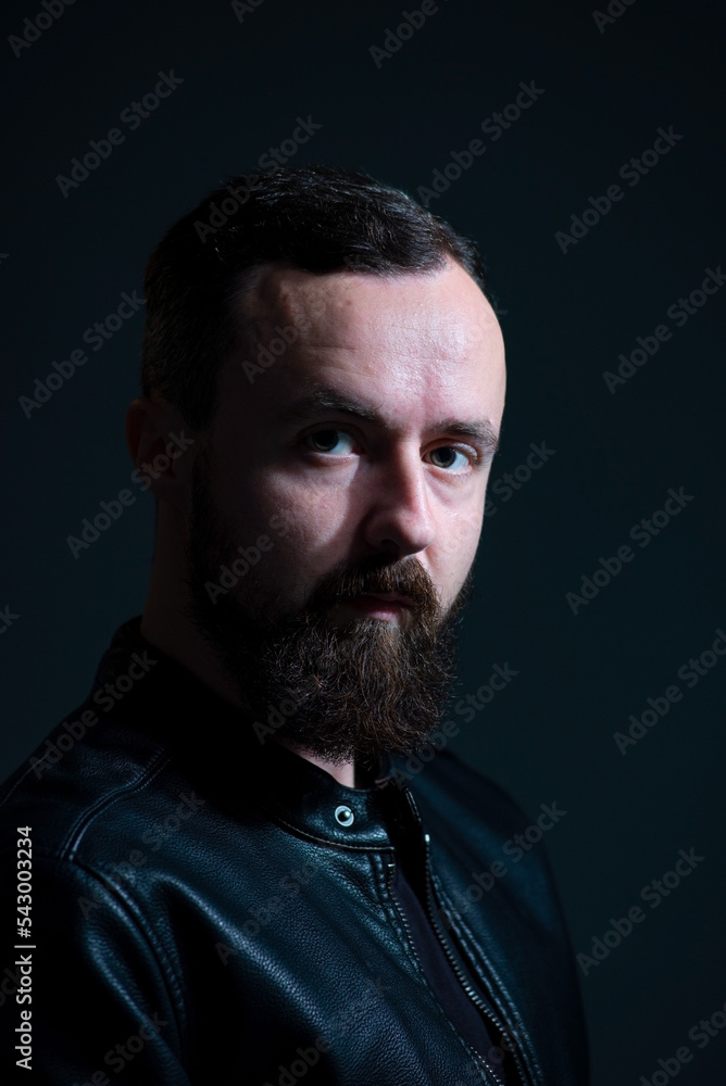 dramatic portrait of bearded millennial guy in leather jacket on dark background