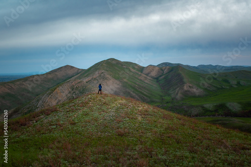 Man standing on the hill with mountains under blue cloudy sky on the background