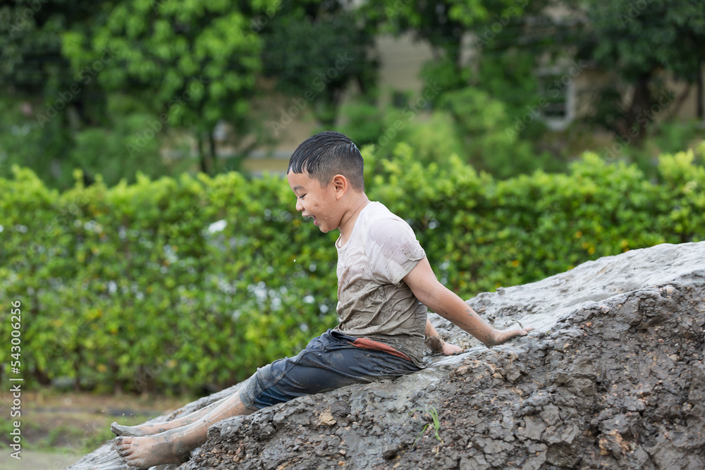 Happy Asian little child boy playing on heap of wet soil during raining in rainy season Happy Asian little child boy playing on heap of wet soil during raining in rainy season