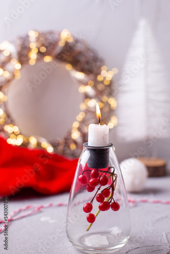 Christmas decorations in  golden and red . White burning candle in holder, Santas hat, fairy lights on wreas on grey textured background. Norven minimalistic style. Still life. photo