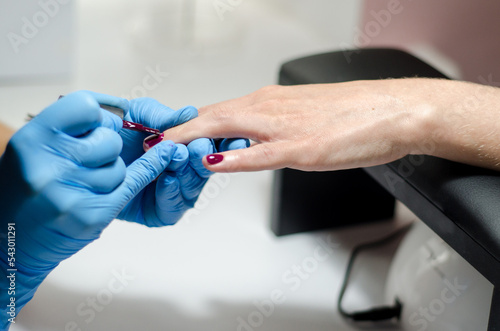 Female manicurist in blue gloves works with young hands and nails under a bright lamp. Process of applying gel polish on nails