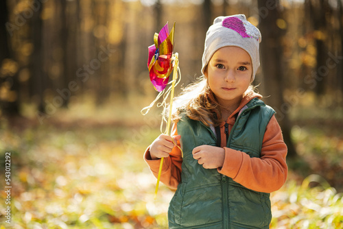 Autumn outdoor portrait of beautiful happy child girl in forest with windmill stick.