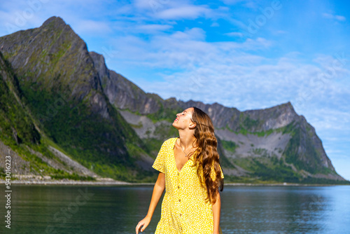a beautiful girl in a yellow dress sunbathes on a beach surrounded by mighty mountains on the island of senja in norway, holiday in the norwegian fjords, steinfjord