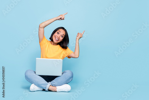 Full body photo of lovely young lady korean excited point empty space netbook dressed stylish yellow look isolated on blue color background © deagreez