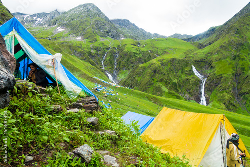 July 14th 2022, Himachal Pradesh India. Multiple colorful tents at Bheem Dwari base camp with beautiful mountains peaks and waterfalls in the background. Shrikhand Mahadev Kailash Himalaya Yatra.