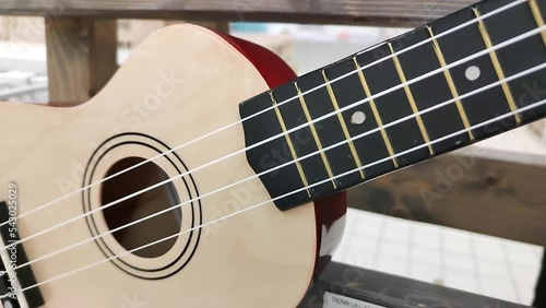 New little guitar in shop window. Stringed musical instrument ukulele on wooden stand. Guitar strings close-up. Hawaiian four-stringed variety of guitar. Ukulele neck fingerboard closeup dolly shot