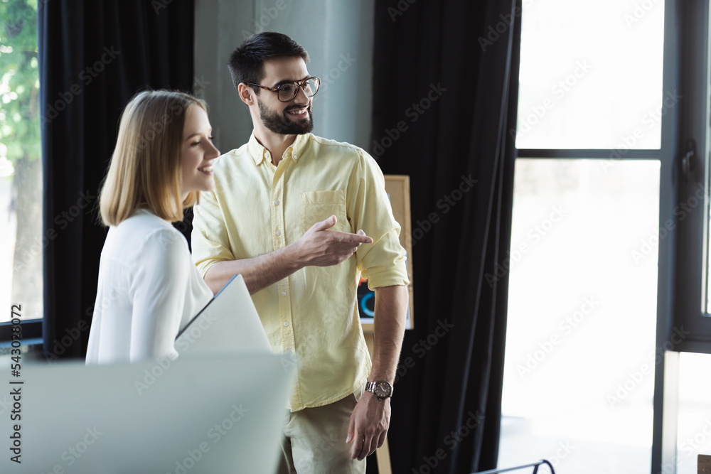 Smiling manager pointing with finger near employee with laptop during internship in office. Smiling manager pointing with finger near employee with laptop during internship in office.