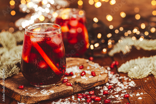 A glass of pomegranate cocktail with orange on the background of Christmas decorations and lights. Festive winter drink