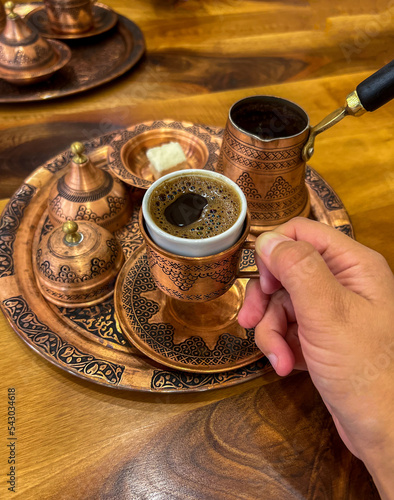 Turkish coffee in hand, traditional authentic copper turkish coffee cup, arabic pot photo