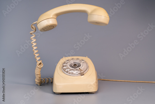 Old beige aged rotary telephone with removed hanging receiver on grey background. Vintage landline home phone with dial, twisted cable and reciever handset. Photo in retro style. photo