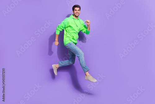 Full length photo of good mood man wear green jumping high running fast isolated purple color background © deagreez