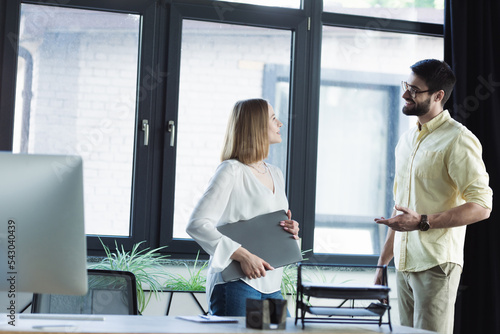 Positive manager talking to employee with laptop during internship in office.