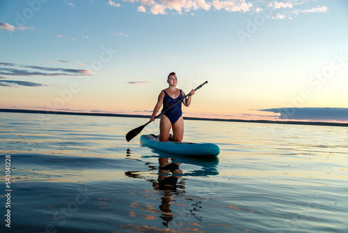 A woman with a short haircut in a swimsuit on a SUP board with a paddle floats on the water. © finist_4