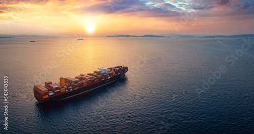 Fototapeta Naklejka Na Ścianę i Meble -  Aerial view of a large, heavy loaded container cargo ship sailing over calm sea into the sunset with copy space