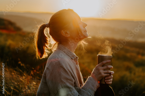 Silhouette of a woman enjoying hot cup of tea on hill at sunset	 photo