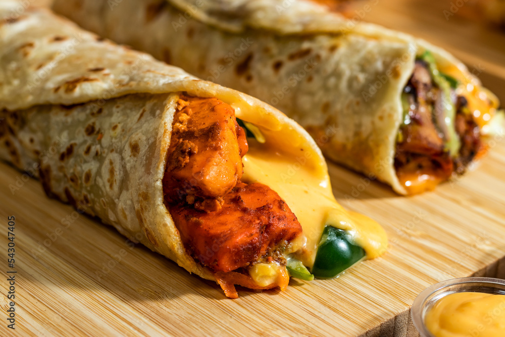Melt Cheese Paneer Wrap, Chicken Afghani Kebab shawarma Wrap with salad dip and sauce isolated wooden board side view of fastfood Melt Cheese Paneer Wrap, Chicken Afghani Kebab shawarma Wrap with salad dip and sauce isolated wooden board side view of fastfood
