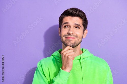 Photo of optimistic attractive guy brunet hairdo dressed green hoodie look empty space hand on chin isolated on purple color background