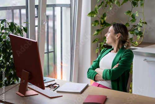 Konstfotografi Young businesswoman sits at wooden table and looks at window with houseplant