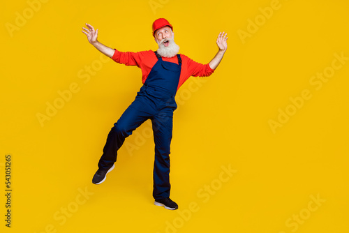 Photo of cheerful good mood senior guy dressed uniform overall red hardhat having fun dancing isolated yellow color background