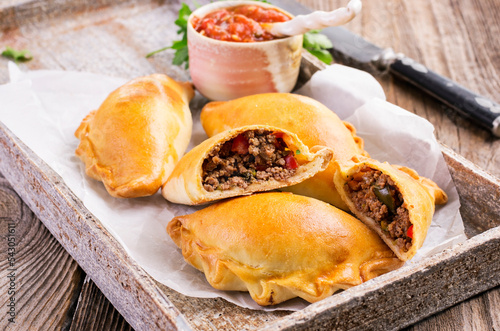 Traditional Spanish baked empanada de carne with minced meat and vegetable served as close-up on a design tray photo