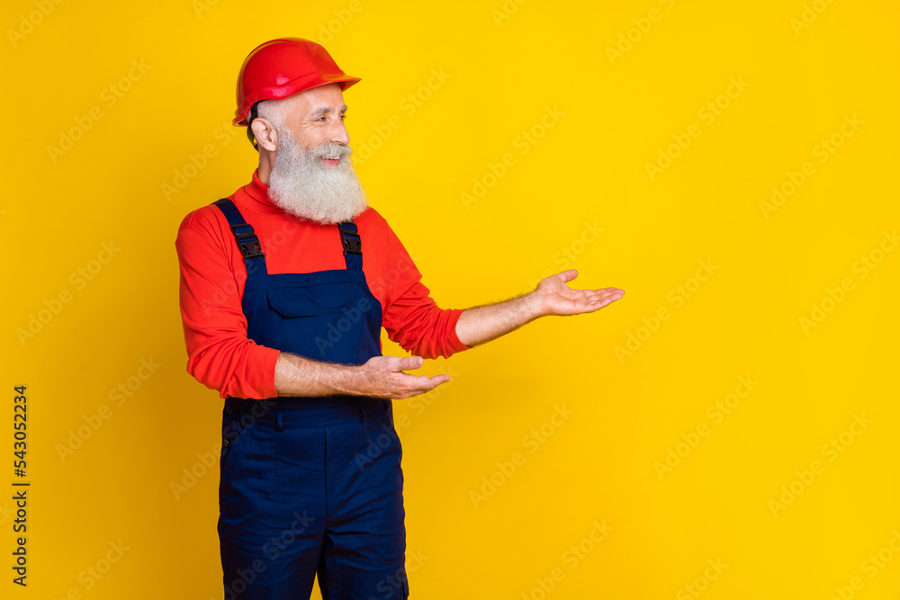 Photo of positive cheerful age man workwear overall red hard hat inviting amrs empty space isolated yellow color background