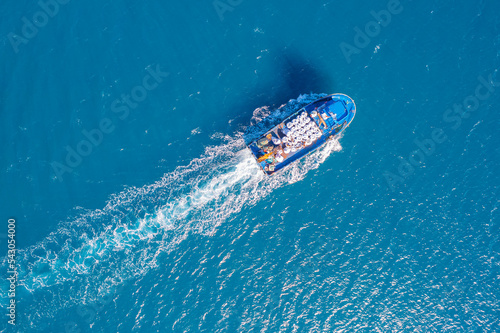 Small cargo ship sails through blue sea to serve fish farm, aerial top view © Parilov