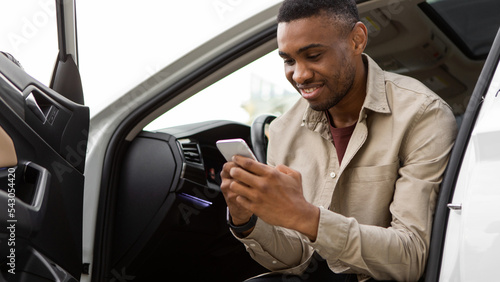 Happy smiling man typing a message on the phone while sitting in the car. © Home-stock