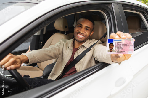  Happy young african man showing his driver's license from open car window