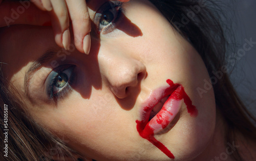 Blonde woman with green eyes acting like a Vampire for Halloween's Day.
Bloody lips in the sun light