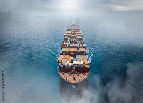 Aerial top view of a big cargo container ship traveling over the calm ocean with fog and clouds