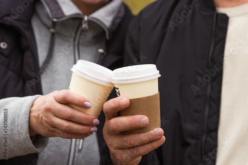 Old man and woman holding paper disposable cups of coffee in hands. Senior couple drinking coffee in autumn park.