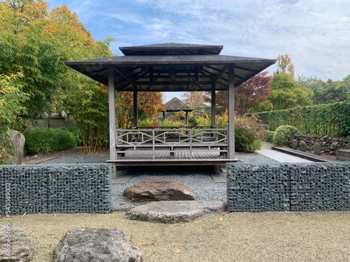 Japanese tea gazebo on a wooden platform in the autumn garden. Gabions and boulders on a flat area of fine gravel. Appeltern, Netherlands, October 12, 2022 photo