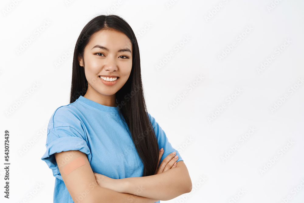 Covid-19, pandemic and healthcare. Smiling korean woman with band aid on shoulder, promotes vaccination, coronavirus vaccine, stands over white background Covid-19, pandemic and healthcare. Smiling korean woman with band aid on shoulder, promotes vaccination, coronavirus vaccine, stands over white background