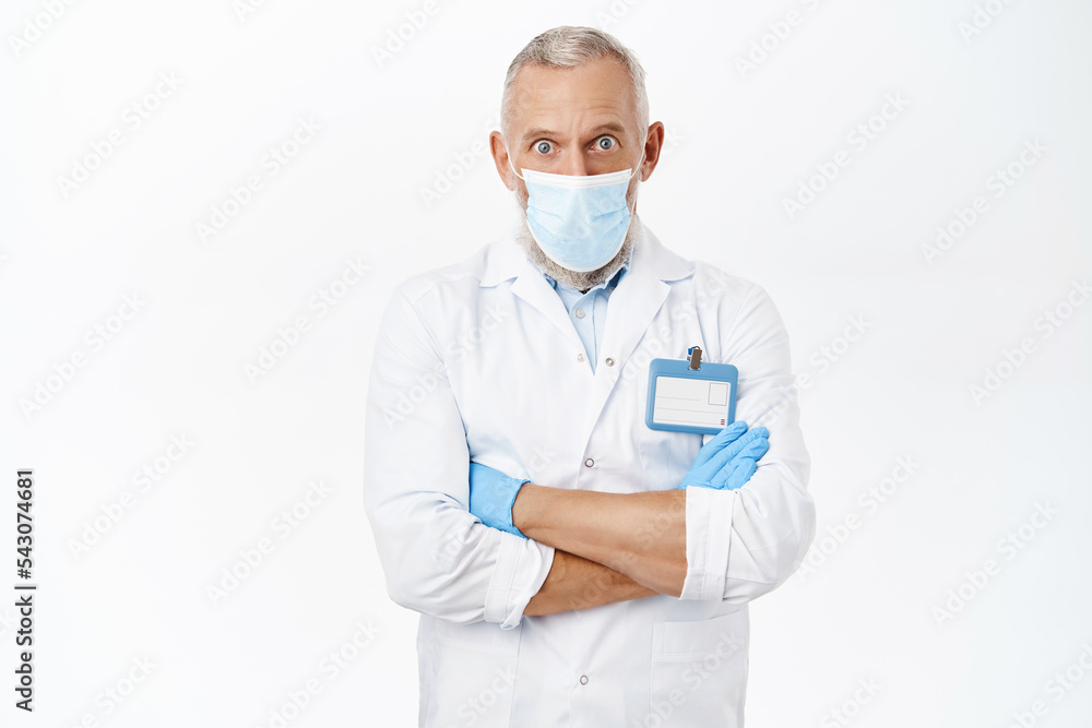 Coronavirus and health concept. Handsome doctor in medical face mask, cross arms on chest, standing in power professional pose, white background