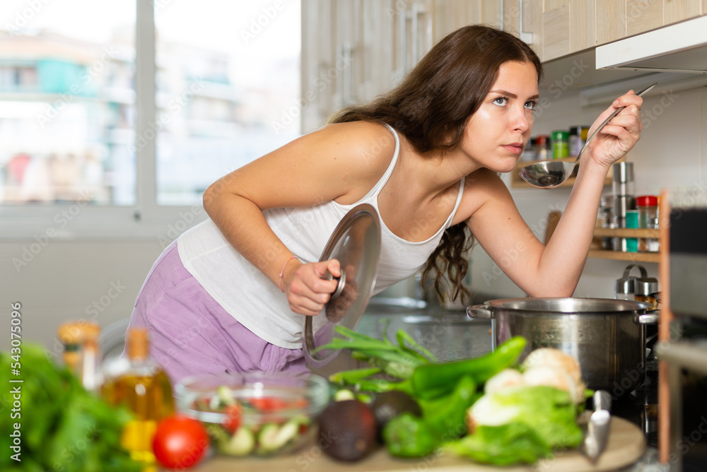 Portrait of young positive woman with saucepan of tasty hot soup in kitchen, cooking concept