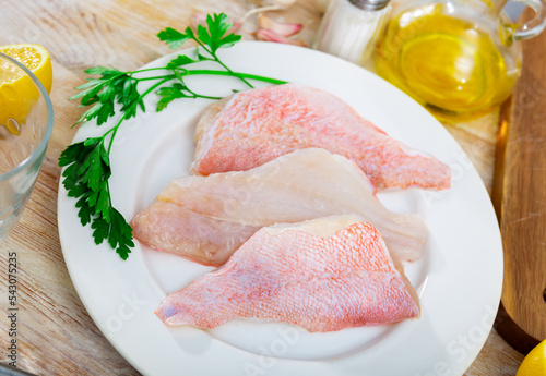 Raw rockfish fillet on plate, garlic, parsley and salt on wooden table. Ingredients for cooking photo