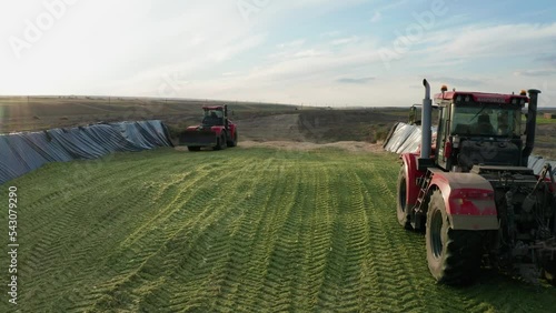 Two Red Tractors Tamp Silage in the Silo Trench. Forage For Animals.Ensiling Is a Bookmark and Storage of Forage Crops without access of Air for Fermentation and later Feeding to Livestock. photo
