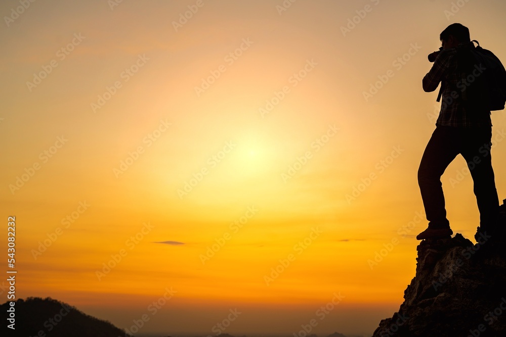 A silhouette of a photographer standing at the top of a mountain in the evening photographing the sunset.Concept of photographer and adventure travel photography